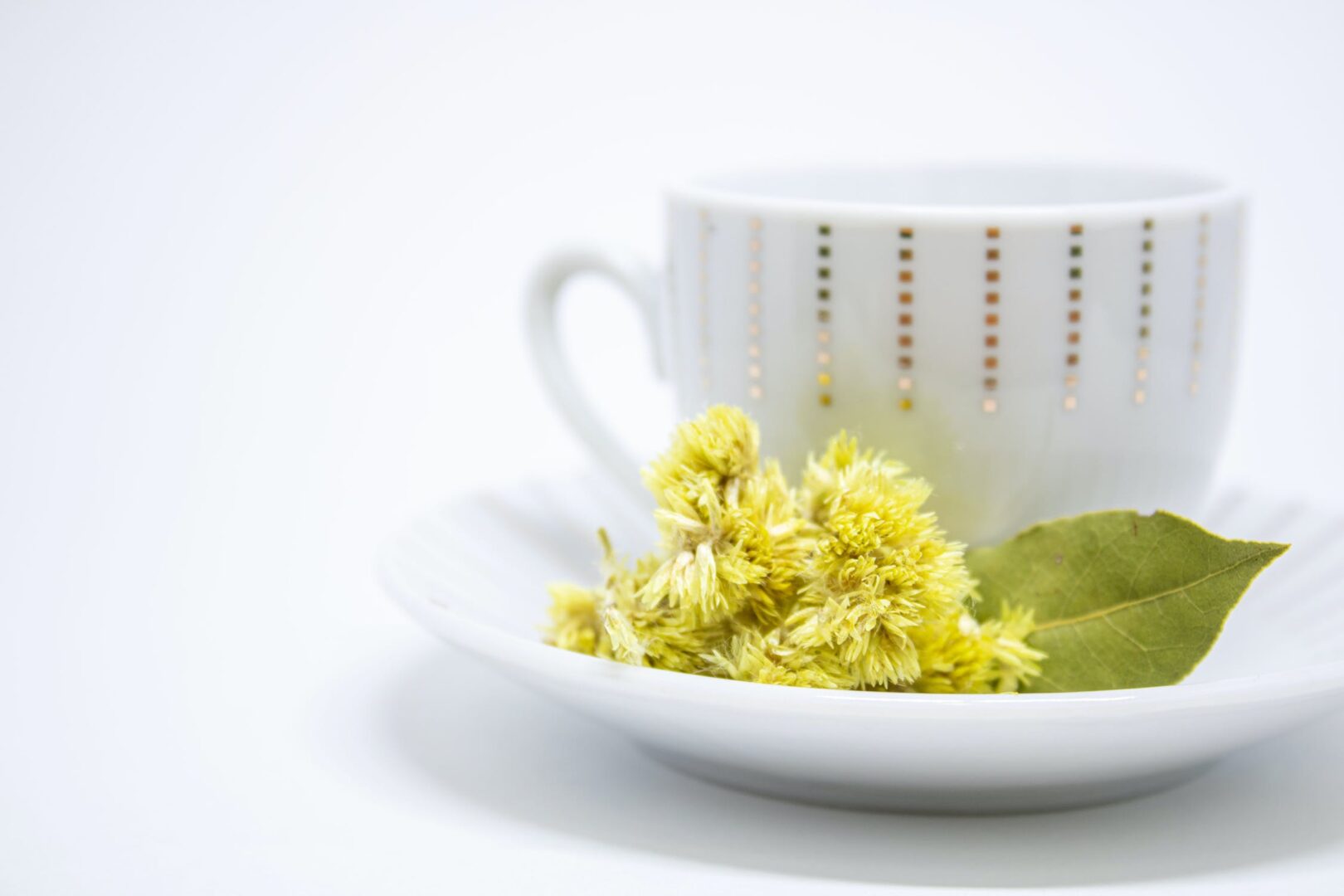 A white cup and saucer with yellow flowers on it.